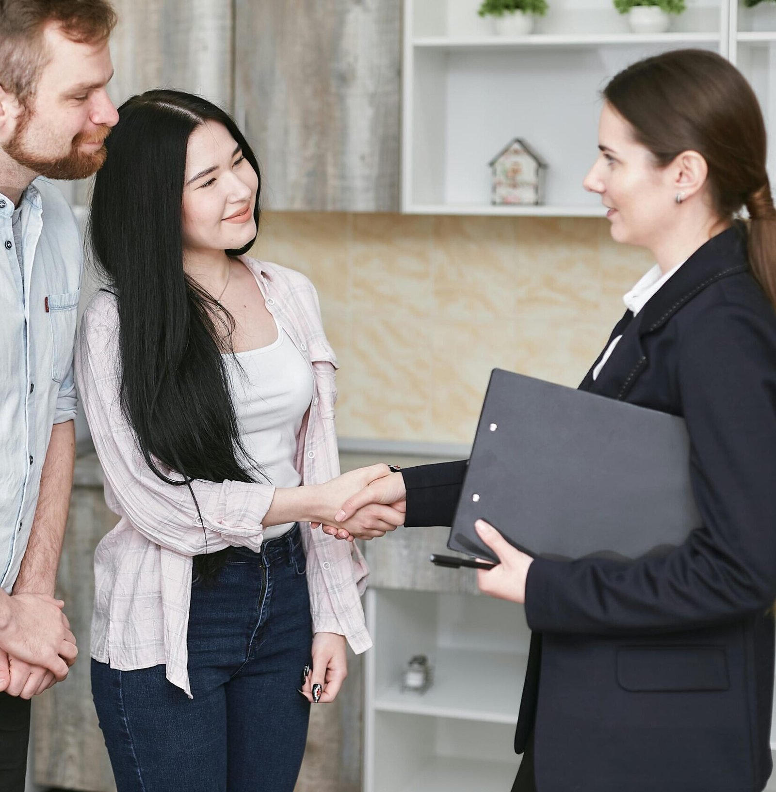 A young couple shakes hands with a real estate agent during a home tour or negotiation in a modern setting.
